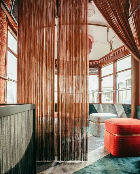 Итальянский дизайнер Кристина Челестино вывела дизайн на улицы Милана в буквальном смысле: вместо того, чтобы оформить инсталляцию в одном из десятков выставочных пространств города, она переделала интерьер старого трамвая 1928 года и пустила его по кольцевому маршруту в районе Брера. В этом передвижном салоне под названием «Tram Corallo» — ностальгическая обстановка с занавесками из нитей, бархатными диванами, латунными деталями и плотными орнаментальными тканями Rubelli.